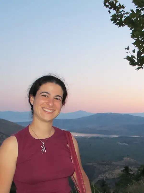 Photo of Darcy Krasne wearing a red tank top with a sunset behind her