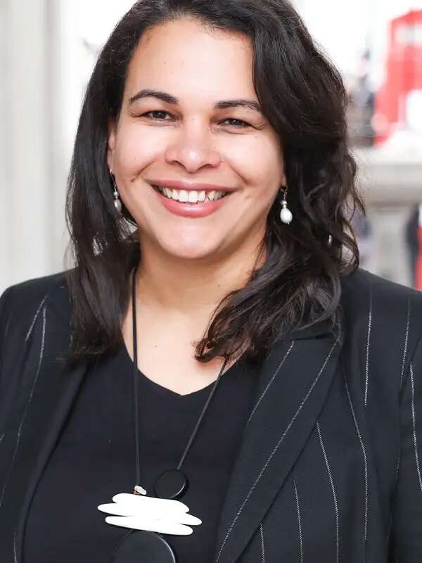 Rosa Andujar smiling at the camera wearing a black top with a blazer and small dangling pearl earrings